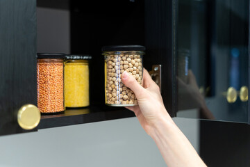 woman take food container with chickpeas from dark wood cupboard, closeup