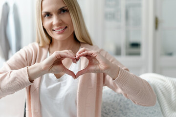 Female making heart shape gesture, hold united fingers close to breast