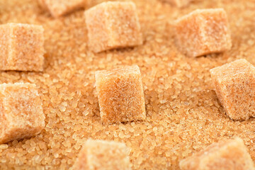 Brown sugar cubes on cane sugar crystals, close up. Demerara golden sugar.