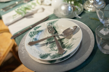 Festive christmas table setting with white and green color plates, tableware, glasses and candles and holiday season decor.	