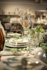Festive christmas table setting with white and green color plates, tableware, glasses and candles and holiday season decor.	