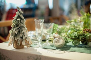 Festive christmas table setting with white and green color plates, tableware, glasses and candles and holiday season decor.	