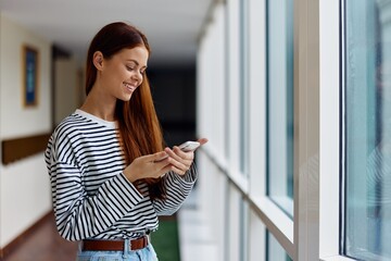 A woman smiling with teeth with red hair with a phone in her hands looks at her smartphone and writes a message, communicating through social media online technology