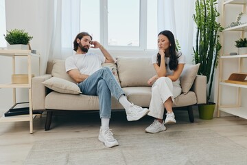 A young married couple sitting on the couch not talking to each other, family quarrels and discontent. Lifestyle in misunderstanding and unwillingness to work on the relationship for love