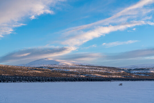 Couple walking with their dog and person on snowmobile in the background on  frozen Fish Lake in winter; Whitehorse, Yukon, Canada