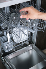 Housework open dishwasher and man putting a glass in the machine. High quality photo