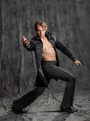An attractive young man in a fantasy camisole, posing in the studio on a gray fabric background. Epic bare-chested pose