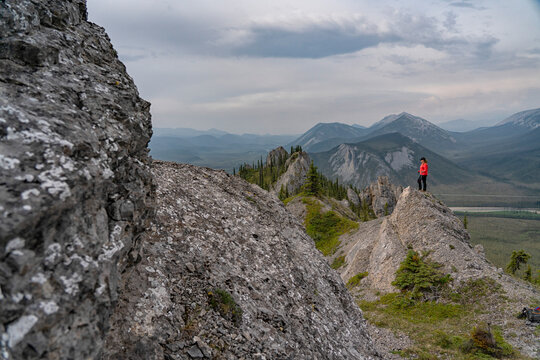 Woman with a walking stick standing on the ridges of Sapper Hill along the Dempster Highway, looking out at the mountain views; Yukon, Canada