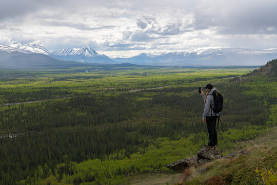 Woman standing overlooking the Ibex Valley just outside Whitehorse, Yukon. Summer has settled in as the landscape is a lush green; Whitehorse, Yukon, Canada