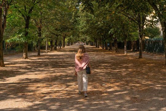 Woman walking down a tree lined path in Paris, France; Paris, France