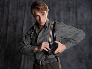 A lawyer with a pistol in a holster, gray shirt and trousers with suspenders, retro style. A young...