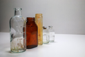 One glass test tube, one amber glass medical pill bottle, two clear glass vaccine bottles, and one small amber vaccine bottle on a white back ground.