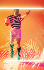 Caucasian female rugby player with ball jumping over illuminated rectangle and plants