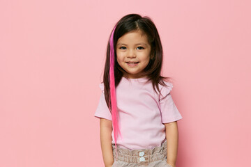 a cute, funny girl stands in stylish clothes holding her hands in her pockets and looks into the camera. She has a pink streak in her hair. Photography with empty space for advertising mockup insert