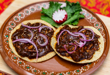 Tostadas de mole poblano, cebolla morada, lechuga, rábano y ajonjolí, en un plato de barro decorado, platillo mexicano típico y tradicional.