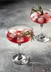 Two glasses of Pomegranate iced cocktail with rosemary on gray textured background isolated close up. Xmas or Valentine's drink