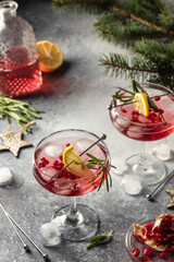Two glasses of pomegranate Christmas iced cocktail with rosemary and lemon on gray textured background. Xmas festive party drink