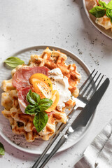 Cheese or potato savory waffles served with yellow tomatoes, cream cheese, ham and bazil leaves with cutlery. Delisious savory breakfast close up. Top view, flat lay