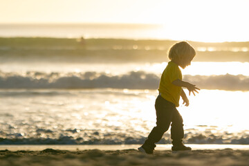 Fototapeta premium Blond little boy walking on the beach by the ocean