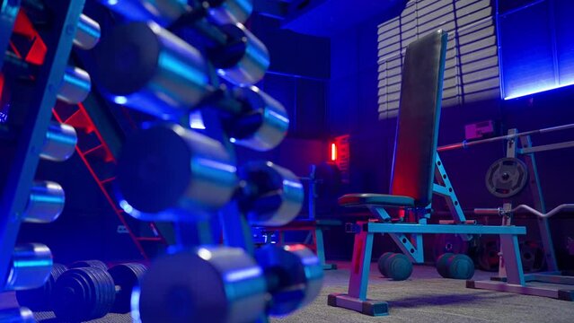 Rack with dumbbells, crossbar, barbell and weights, sports bench and kettlebell in an empty gym with blue and red lights. Sports equipment for sports, bodybuilding, fitness, crossfit and powerlifting.