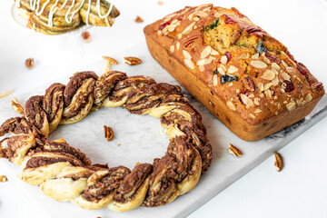 Close up de pan de frutas con cerezas acompañado de trenza de chocolate de avellana acompañada de nueces en mesa de marmol 