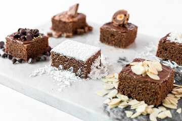 Fototapeta na wymiar Brownies de chocolate decorados con azúcar, almendras, chocolate, coco, chispas de chocolate y avellana en una mesa de marmol. 