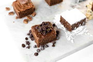 Brownies de chocolate decorados con azúcar, almendras, chocolate, coco, chispas de chocolate y avellana en una mesa de marmol. 
