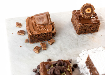 Brownies de chocolate decorados con azúcar, almendras, chocolate, coco, chispas de chocolate y avellana en una mesa de marmol. 