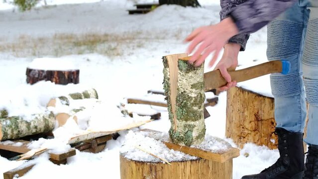A man is chopping firewood with an axe in winter in the snow. Alternative heating, wood harvesting, energy crisis