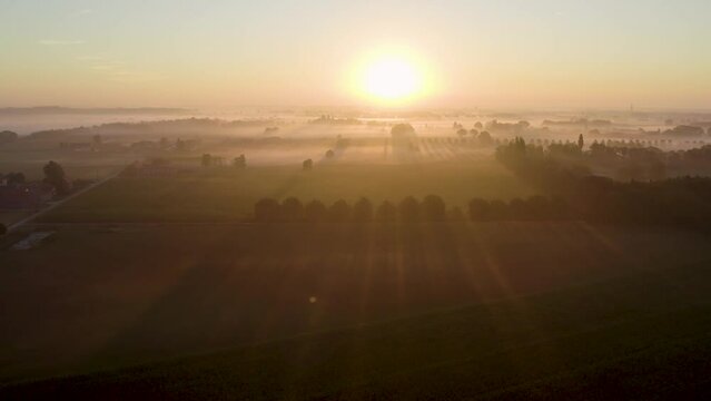 Sunrise morning sun through the fog over the plain and agraric farming fields of the meadow near a rural village with a house and farms, aerial view landscape. High quality 4k footage