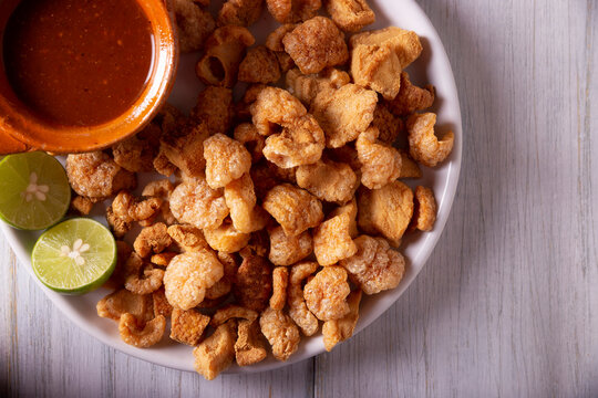Chicharrones. Deep fried pork rinds, crispy pork skin pieces, traditional mexican ingredient or snack served with lemon juice and red hot chili sauce.