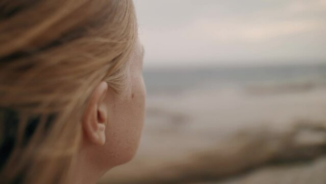 Redhead woman freckles face skin contemplating sea coast landscape dramatic sky closeup slowmo