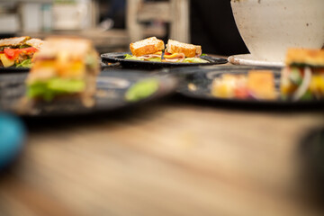 Emparedado de jamón con queso derretido y vegetales
en mesa de madera con un plato negro al fondo.
