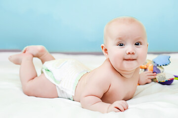 The baby lies on her tummy on the bed with her legs raised. Laying it out on your stomach after sleep. A child in a diaper on a white bed.