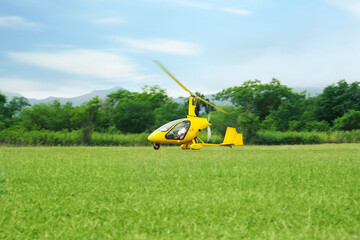 Yellow rotorcraft flying above grass near trees