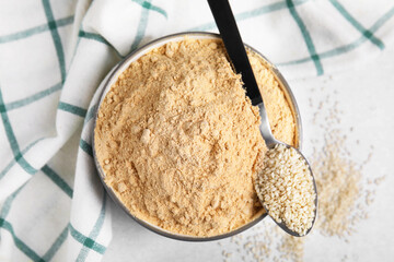 Sesame flour in ceramic bowl and spoon of seeds on grey table, top view