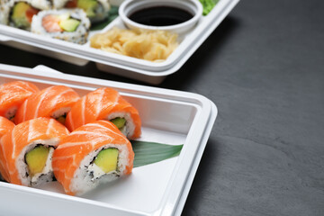 Food delivery. Delicious sushi rolls in plastic containers on black table, closeup with space for text
