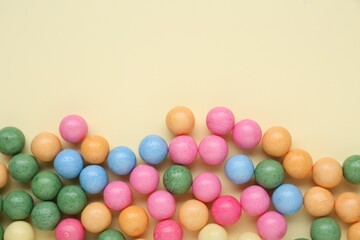 Many bright chewy gumballs on beige background, flat lay. Space for text
