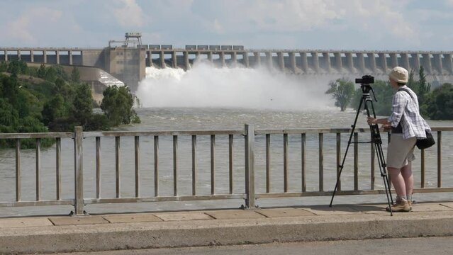 Photographer with tripod takes pictures of hydro dam releasing water