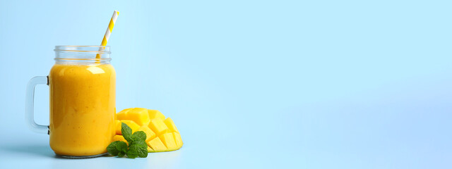Mason jar with delicious fruit smoothie and fresh mango on light blue background, space for text. Banner design