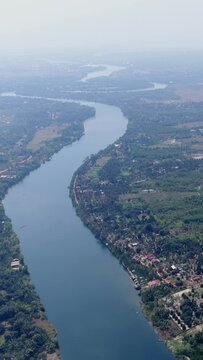 Vertical video of Drone footage of the northern part of Kampot, Cambodia. The camera is showing the Praek Tuek Chhu river with its lush tropical vegetation and the local houses built around it.