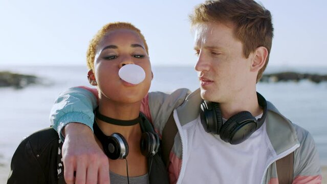 Diverse couple, beach and bubblegum with a playful boyfriend and girlfriend having fun together. Gum, bubbles and popping with a man and woman in love by the sea being silly and playing
