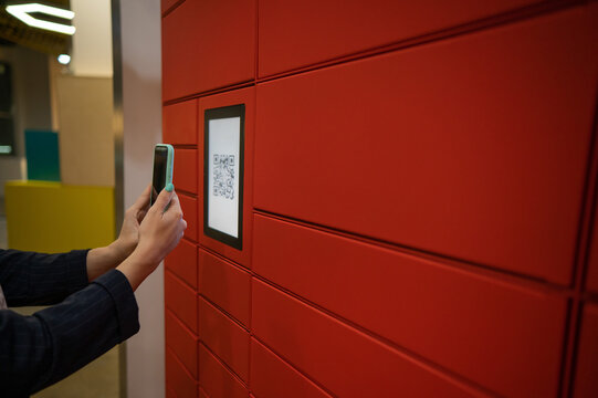 A woman scans a red code to pick up a parcel at a parcel machine. Automated Postal Box.
