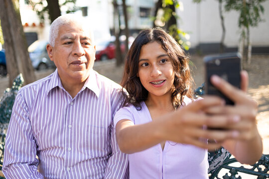 Teen girl and her grandfather taking a selfie outdoors.