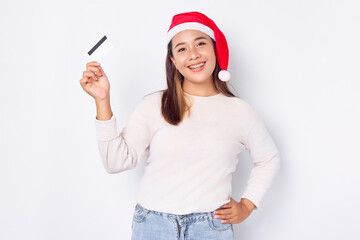 Fototapeta na wymiar Cheerful and excited young Asian woman in a Christmas hat showing a blank white credit card at camera isolated on white background