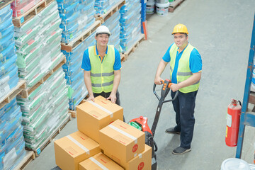 Male warehouse worker pulling a pallet truck warehouse workers wearing helmets and reflective...