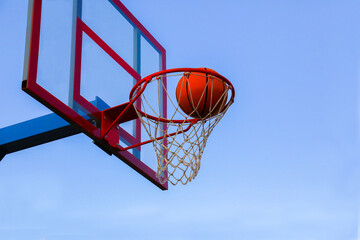 The sport of basketball. A basketball in a basket on an outdoor basketball court