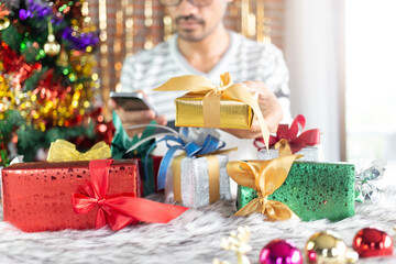man holding and giving gold gift with using smartphone at christmas place and christmas gifts decoration 