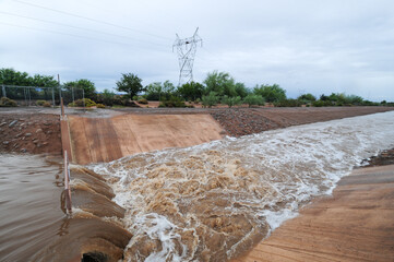 A rainwater runoff canal channeling muddy stormwater through a concrete structure; the rushing...