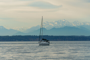 A sailing boat floats in the Puget Sound in Seattle, Washington with a beautiful backdrop of the Olympics mountain range.